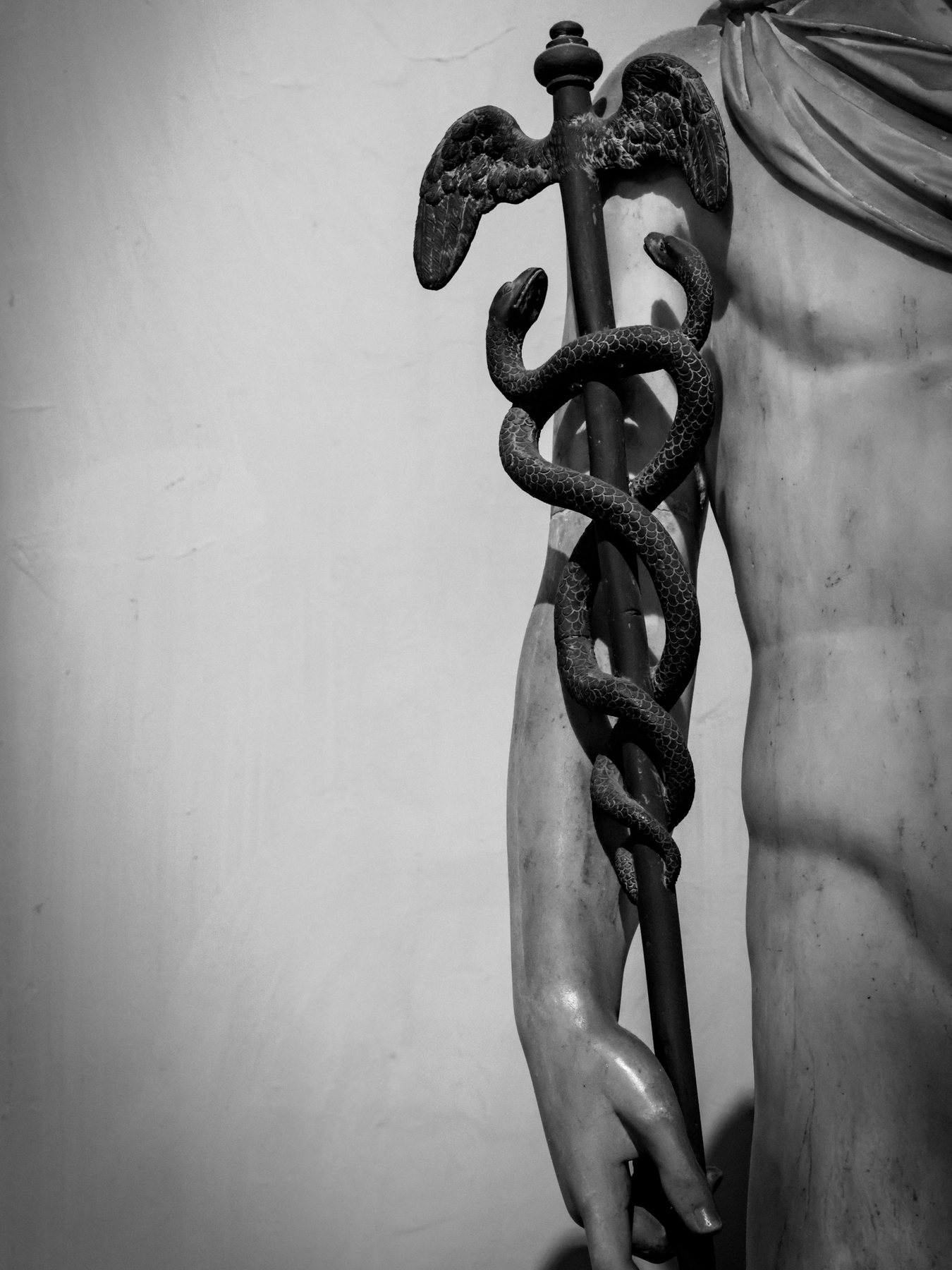 The caduceus of Hermes, a winged staff entwined by two serpents, held by a marble statue